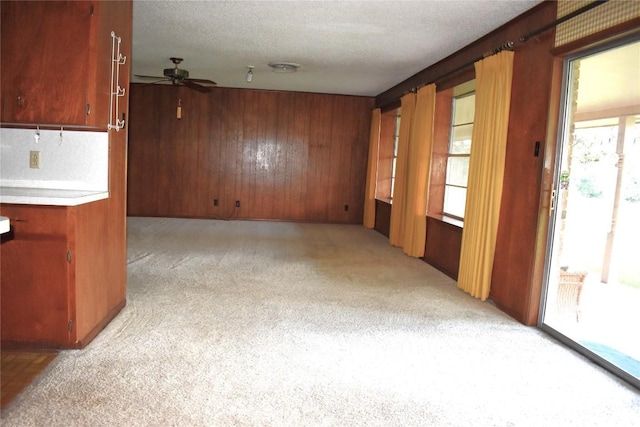 unfurnished room featuring ceiling fan, wooden walls, light colored carpet, and a textured ceiling