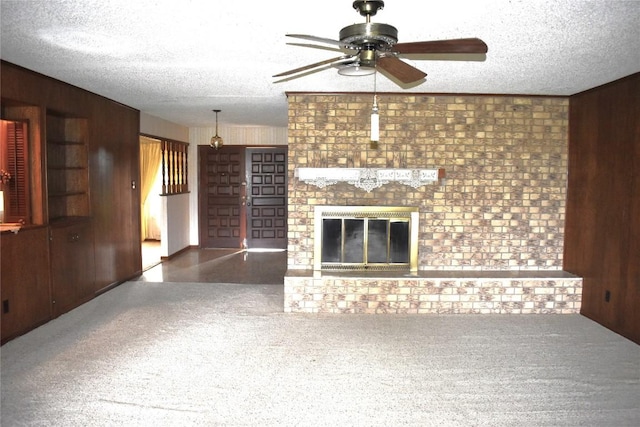 unfurnished living room with wooden walls, carpet, a brick fireplace, and a textured ceiling