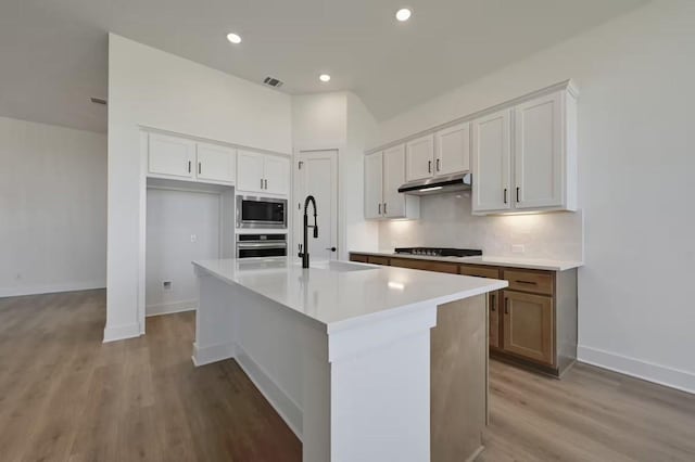 kitchen with white cabinetry, light hardwood / wood-style floors, stainless steel appliances, and an island with sink