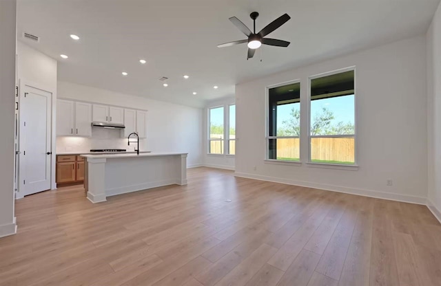 kitchen featuring white cabinetry, tasteful backsplash, light wood-type flooring, ceiling fan, and a kitchen island with sink