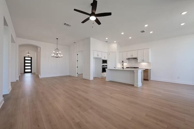 unfurnished living room with ceiling fan with notable chandelier and light hardwood / wood-style floors