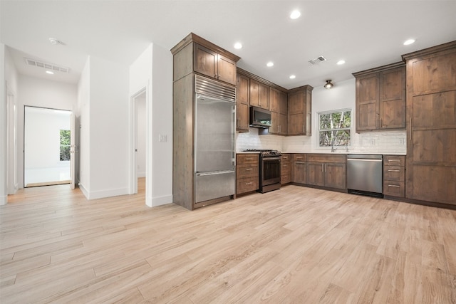 kitchen with stainless steel appliances, light countertops, visible vents, light wood-style flooring, and decorative backsplash