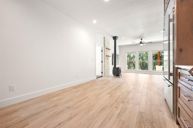 unfurnished living room featuring recessed lighting, a ceiling fan, baseboards, light wood-style floors, and a wood stove