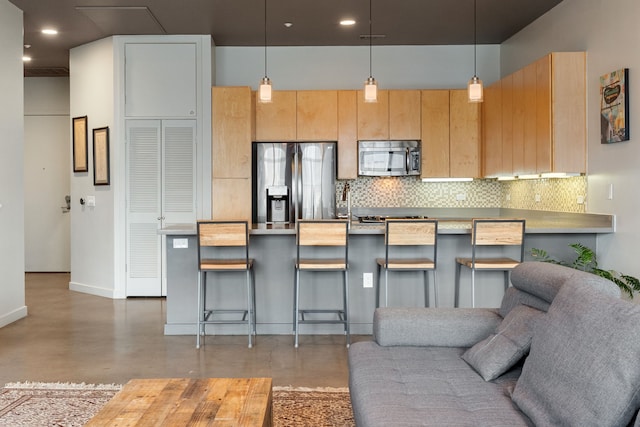 kitchen with stainless steel appliances, concrete floors, a breakfast bar, decorative light fixtures, and backsplash