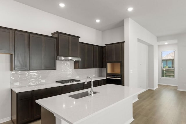 kitchen with oven, stainless steel gas cooktop, a kitchen island with sink, and sink