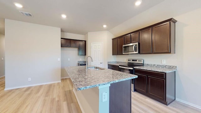 kitchen featuring appliances with stainless steel finishes, light wood-type flooring, light stone counters, sink, and a center island with sink