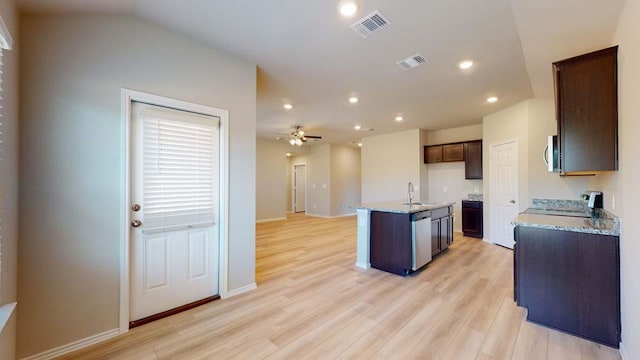 kitchen with a center island with sink, sink, ceiling fan, light stone countertops, and light wood-type flooring