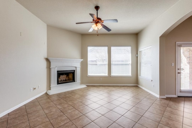 253 Lear Ave, Buda, TX 78610 - unfurnished living room featuring a ceiling fan, a fireplace with raised hearth, arched walkways, and tile patterned flooring