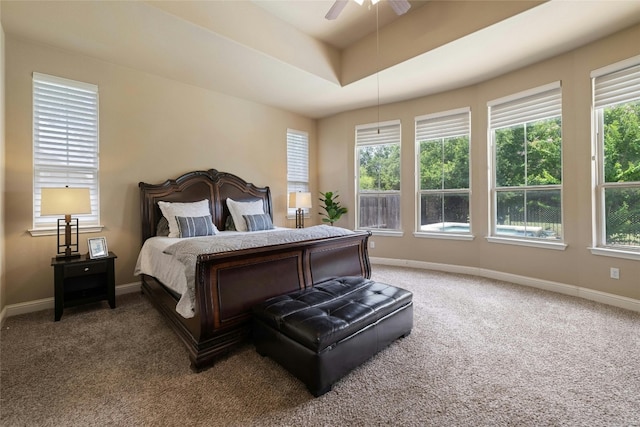 carpeted bedroom with baseboards, multiple windows, a raised ceiling, and ceiling fan