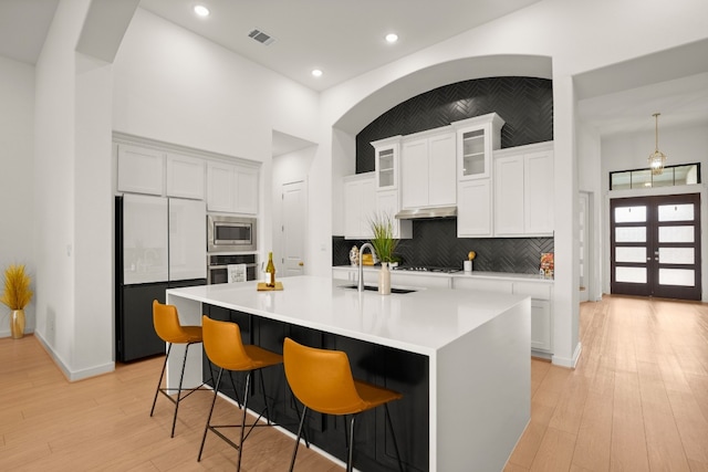 kitchen featuring built in appliances, sink, white cabinetry, and an island with sink