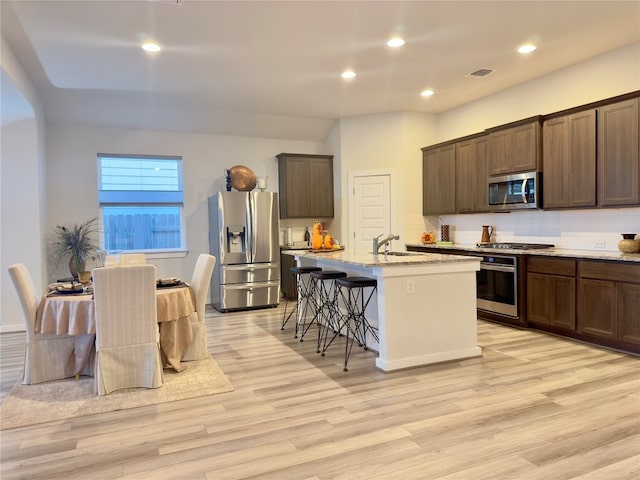 kitchen with sink, a kitchen island with sink, appliances with stainless steel finishes, and light hardwood / wood-style flooring