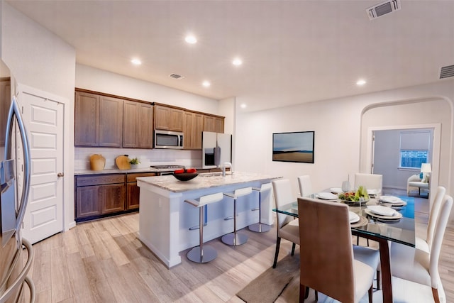 kitchen featuring appliances with stainless steel finishes, sink, backsplash, light wood-type flooring, and a center island with sink