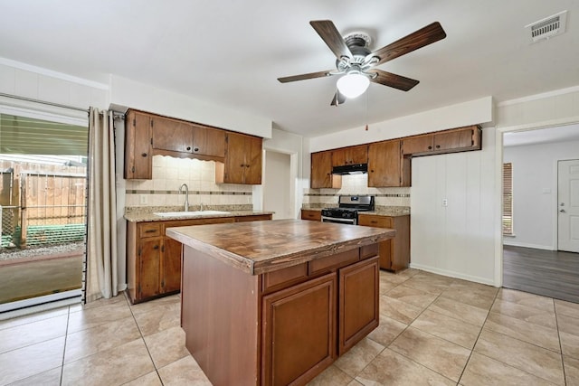 kitchen with gas stove, ceiling fan, sink, decorative backsplash, and a kitchen island