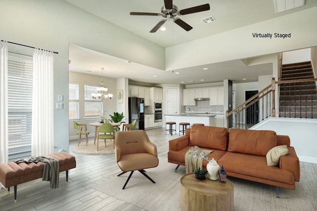 living room with ceiling fan with notable chandelier, light wood-type flooring, sink, and a high ceiling