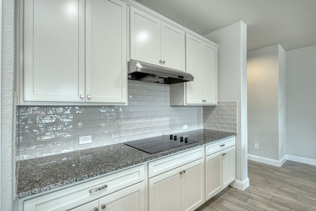 kitchen featuring black electric stovetop, light wood-type flooring, tasteful backsplash, dark stone counters, and white cabinets