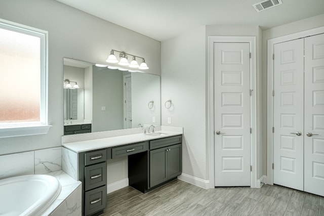 bathroom featuring hardwood / wood-style floors, vanity, and a relaxing tiled tub