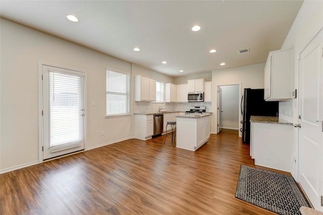 kitchen featuring hardwood / wood-style floors, a center island, appliances with stainless steel finishes, light stone counters, and white cabinetry