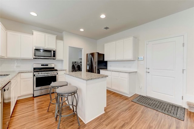 kitchen featuring white cabinets, a kitchen island, separate washer and dryer, light hardwood / wood-style floors, and stainless steel appliances