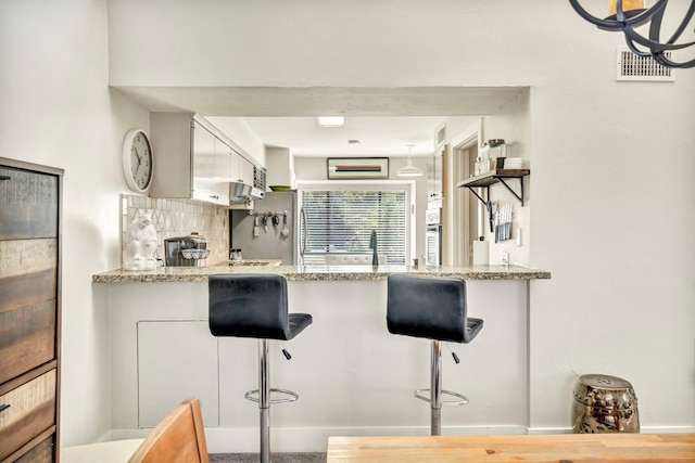 kitchen featuring light stone counters, white cabinets, a kitchen bar, and kitchen peninsula