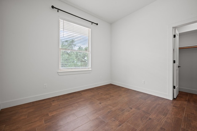 unfurnished bedroom with dark wood-style floors, baseboards, a spacious closet, and a closet