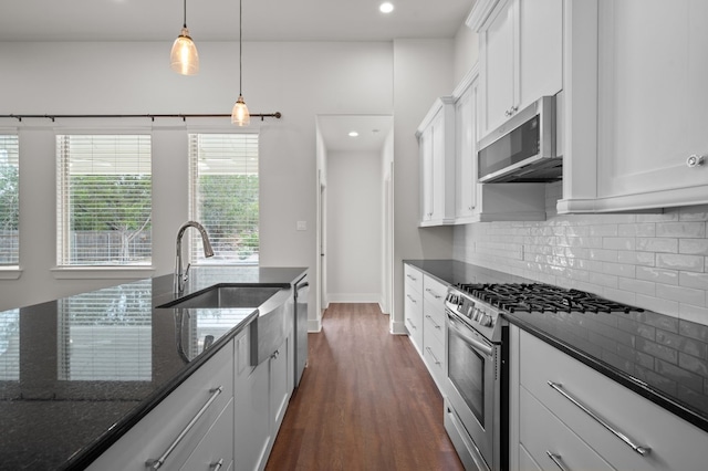 kitchen featuring dark wood-type flooring, dark stone counters, decorative light fixtures, white cabinets, and appliances with stainless steel finishes