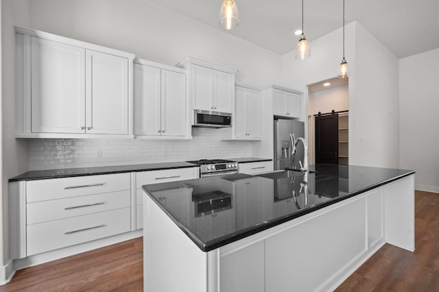 kitchen with white cabinetry, stainless steel appliances, a barn door, dark hardwood / wood-style flooring, and an island with sink