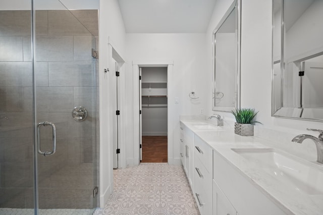 full bathroom featuring a shower stall, double vanity, a walk in closet, tile patterned flooring, and baseboards