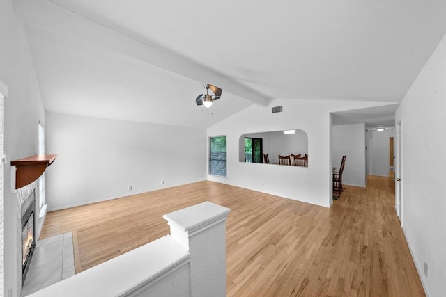 living room featuring ceiling fan, light hardwood / wood-style floors, a tiled fireplace, and lofted ceiling with beams