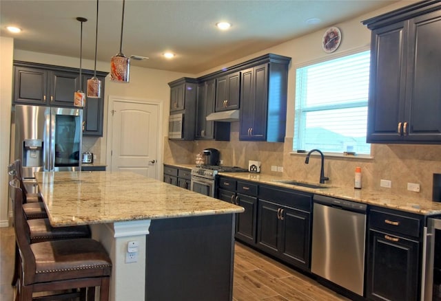 kitchen featuring appliances with stainless steel finishes, sink, light hardwood / wood-style flooring, a center island, and hanging light fixtures