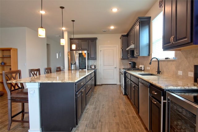 kitchen featuring a center island, hanging light fixtures, sink, appliances with stainless steel finishes, and a kitchen bar