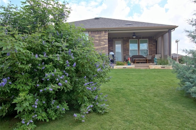 rear view of property with ceiling fan and a lawn