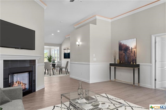 living room with ornamental molding, vaulted ceiling, a tiled fireplace, and hardwood / wood-style floors