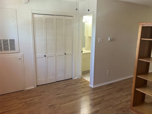 unfurnished bedroom with ensuite bathroom, dark wood-type flooring, a closet, and baseboards