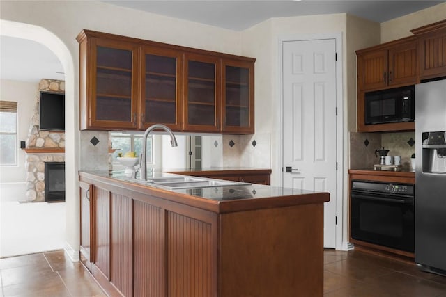 kitchen with black appliances, dark tile patterned floors, a stone fireplace, and kitchen peninsula