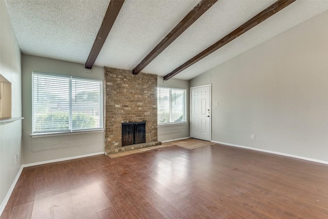 unfurnished living room with a brick fireplace, hardwood / wood-style floors, a textured ceiling, and vaulted ceiling with beams