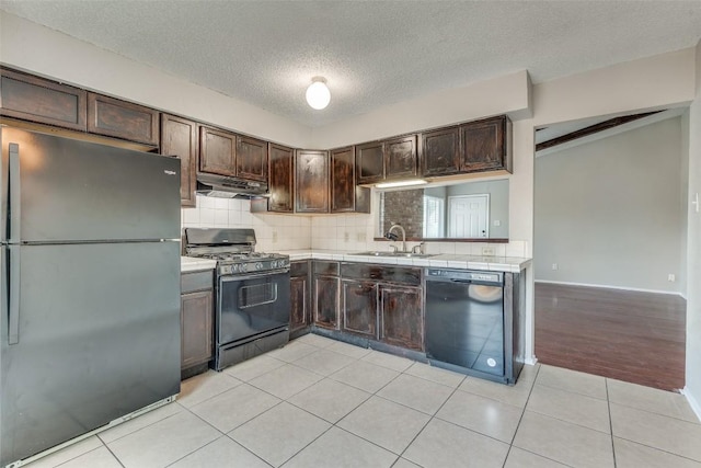 kitchen with tasteful backsplash, sink, light tile patterned floors, dark brown cabinetry, and black appliances