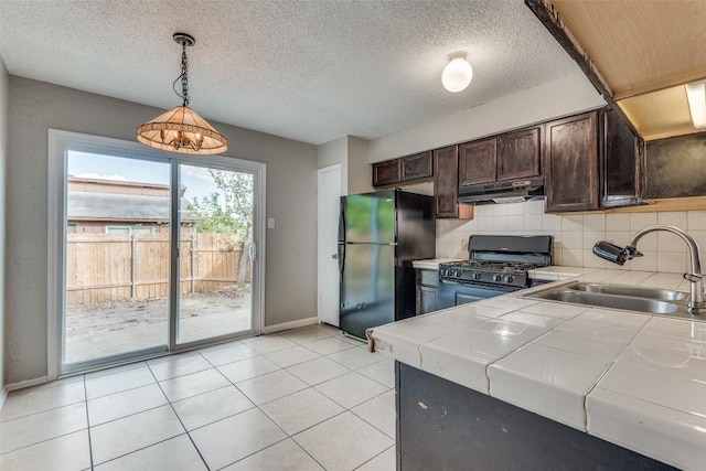 kitchen with sink, dark brown cabinetry, gas range oven, black fridge, and decorative light fixtures