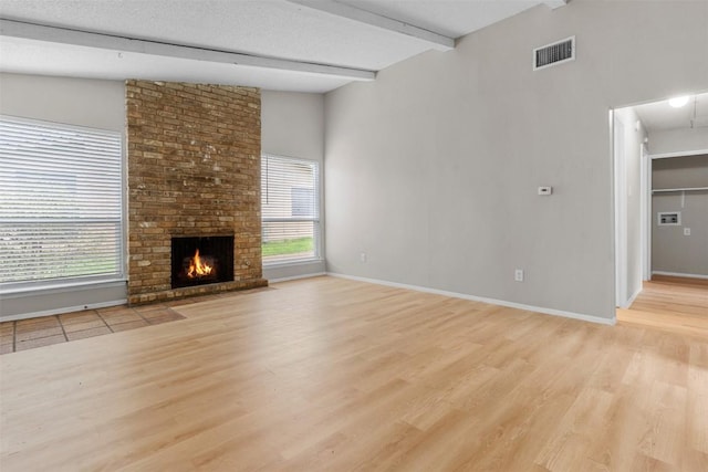 unfurnished living room with a brick fireplace, light hardwood / wood-style flooring, lofted ceiling with beams, and a textured ceiling