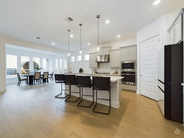 kitchen with appliances with stainless steel finishes, a breakfast bar, pendant lighting, light hardwood / wood-style floors, and an island with sink