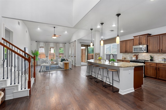 kitchen featuring a kitchen bar, vaulted ceiling, ceiling fan, pendant lighting, and a center island with sink