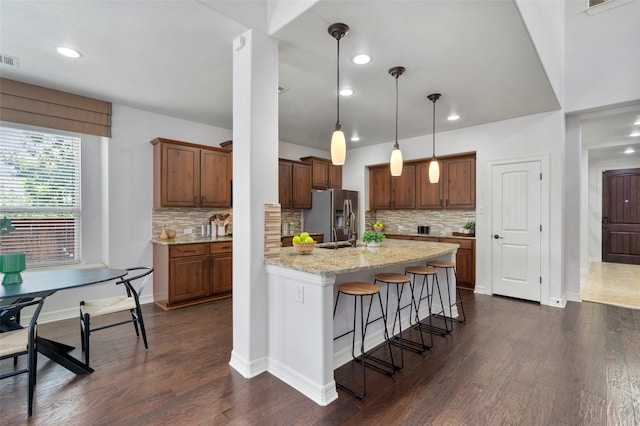 kitchen with pendant lighting, decorative backsplash, stainless steel fridge, and light stone countertops