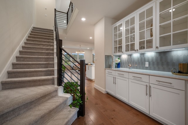 stairs with an inviting chandelier, bar area, and hardwood / wood-style flooring