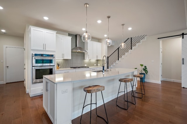 kitchen featuring sink, a center island with sink, wall chimney exhaust hood, stainless steel appliances, and a barn door