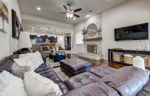 living room featuring dark hardwood / wood-style floors, ceiling fan, and a stone fireplace