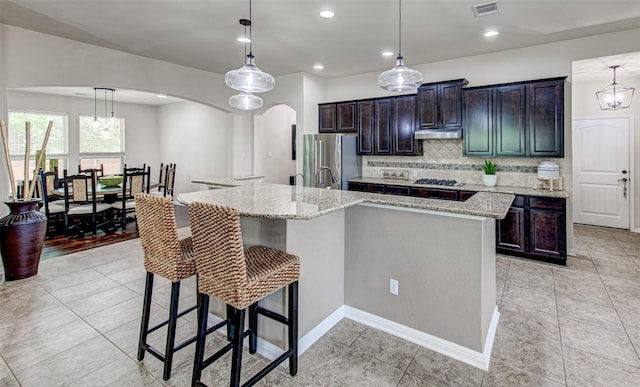 kitchen featuring decorative backsplash, stainless steel fridge, a spacious island, and decorative light fixtures