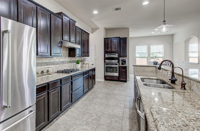 kitchen with light stone countertops, sink, backsplash, decorative light fixtures, and appliances with stainless steel finishes