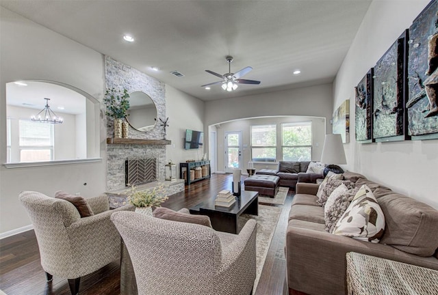 living room with a wealth of natural light, a fireplace, ceiling fan with notable chandelier, and dark hardwood / wood-style floors