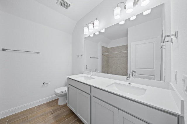 bathroom featuring vanity, tiled shower, hardwood / wood-style floors, toilet, and lofted ceiling