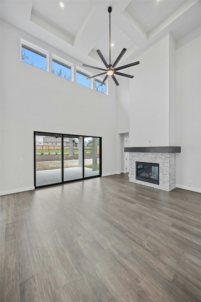 unfurnished living room with ceiling fan, a stone fireplace, hardwood / wood-style floors, and a high ceiling