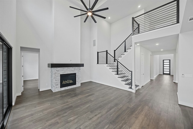 unfurnished living room with dark wood-type flooring, a towering ceiling, a stone fireplace, and ceiling fan